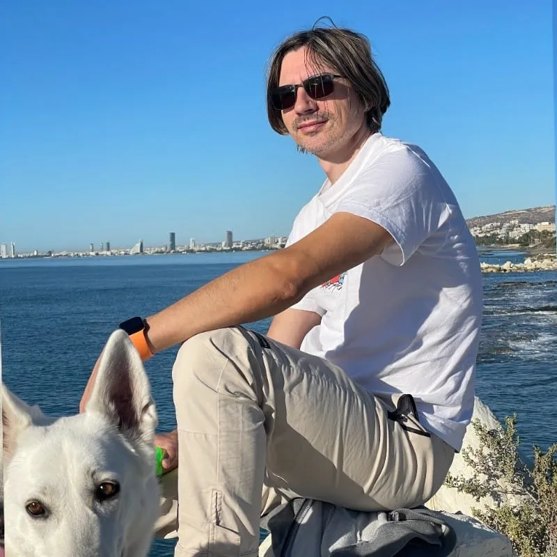 Me in sunglasses sitting on a rock by the sea with a white dog